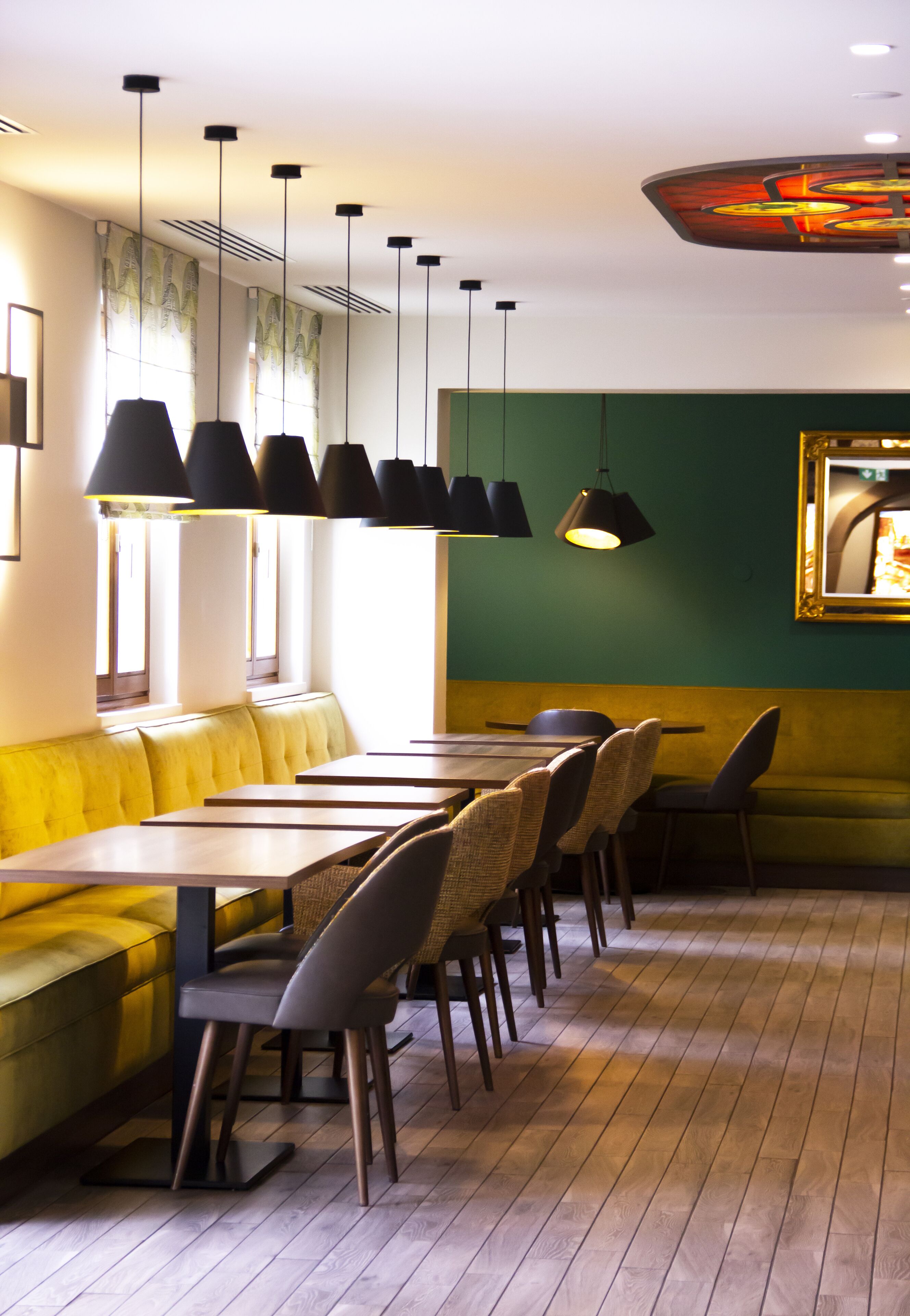 A restaurant with a yellow booth seating area, wooden tables, and black pendant lights.