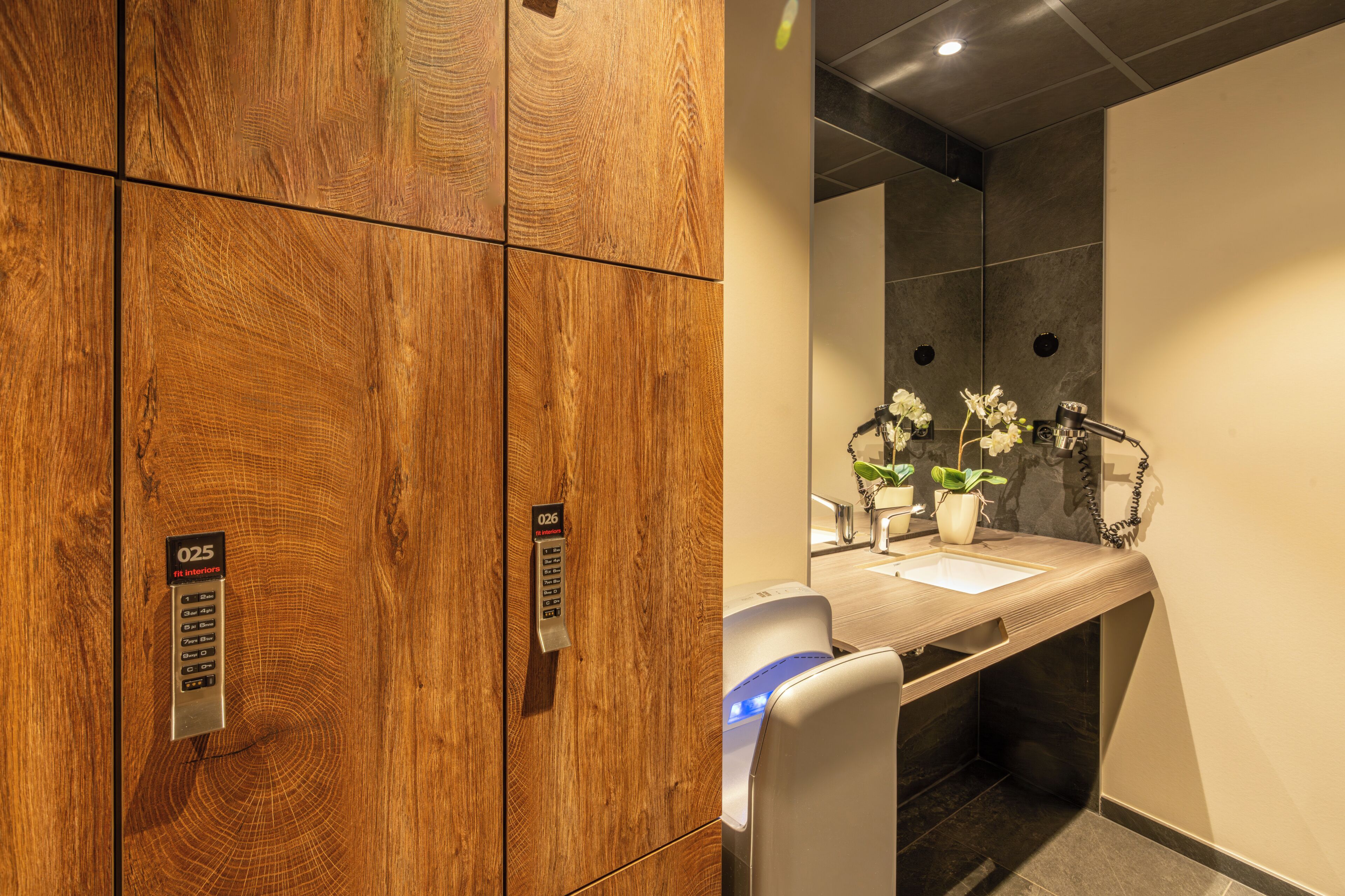 Un mur recouvert de panneaux de bois, doté d’une serrure numérique, un lavabo avec un miroir et une plante.