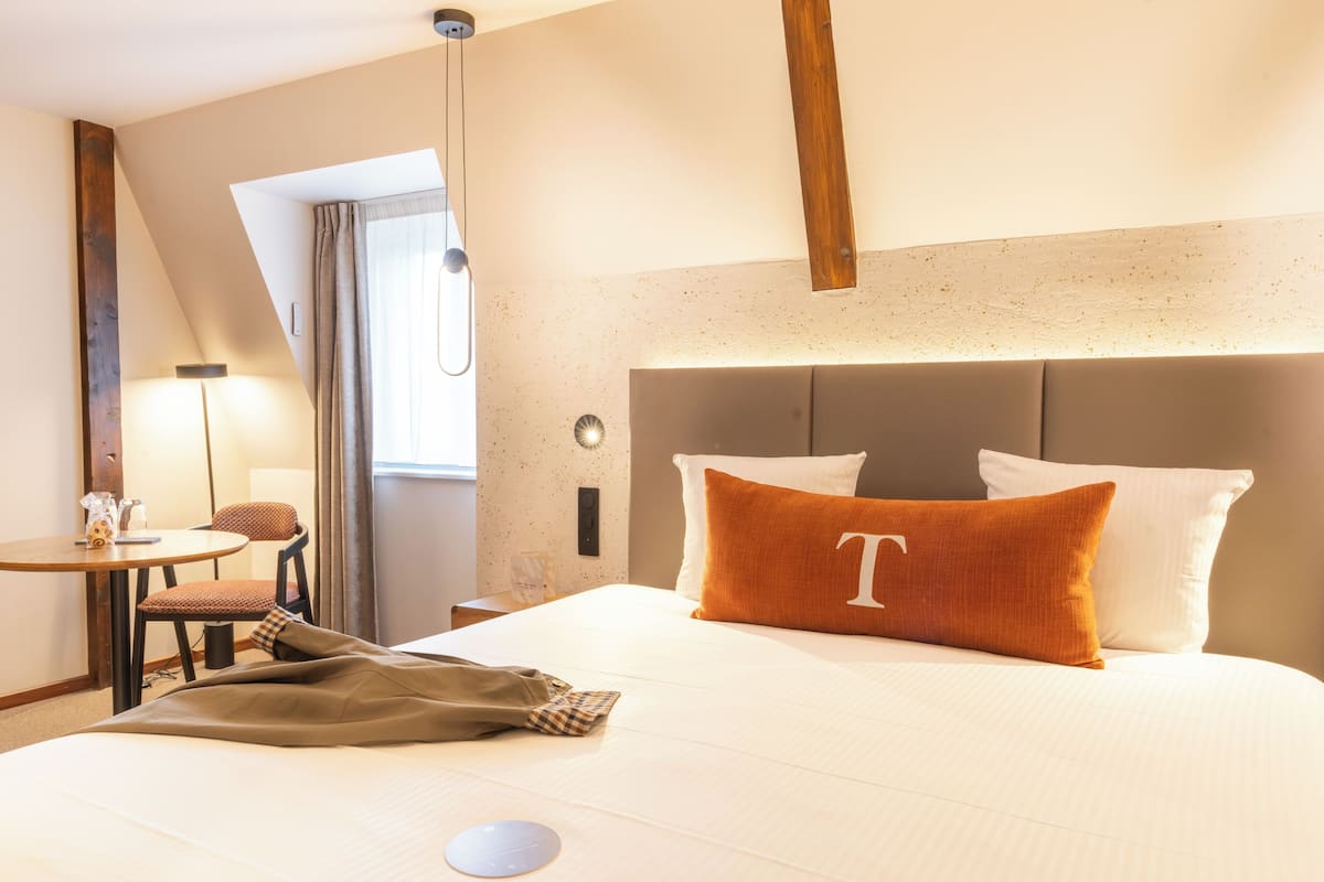 A hotel room with a bed, a bedside table, a chair, and a window with curtains.