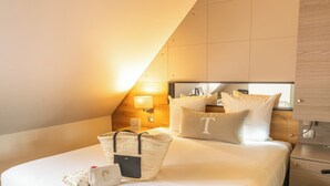 A hotel room with a bed, pillows, a nightstand, a lamp, a mirror, and a wooden headboard. - Hôtel Maison Turenne (Colmar)