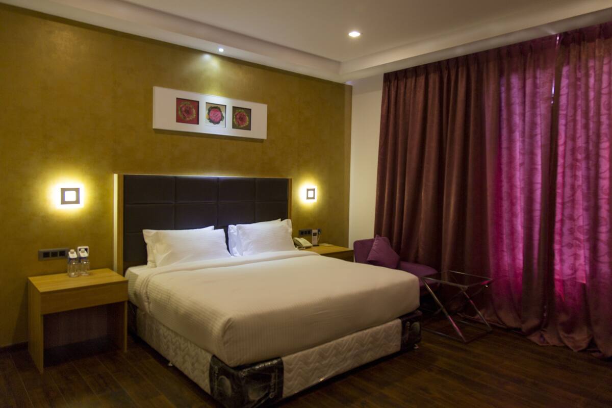 Una habitación de hotel con una cama grande, dos mesitas de noche, una silla y una cortina.