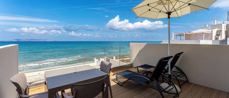 Ein Balkon mit Tisch und Stühlen, einem großen Sonnenschirm und Blick auf das Meer.