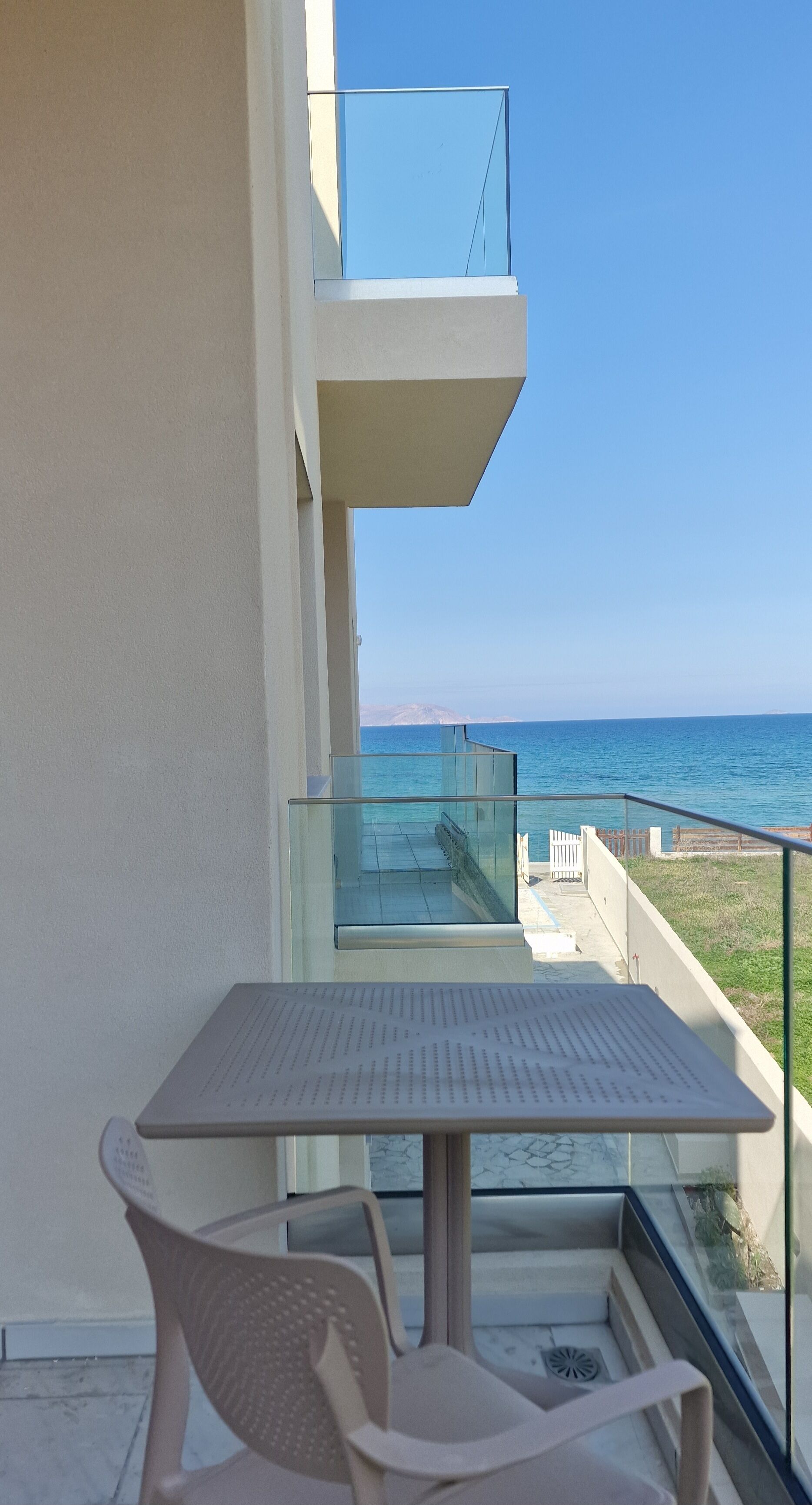 Un balcón con mesa y sillas, con vista a un mar azul y una montaña distante.