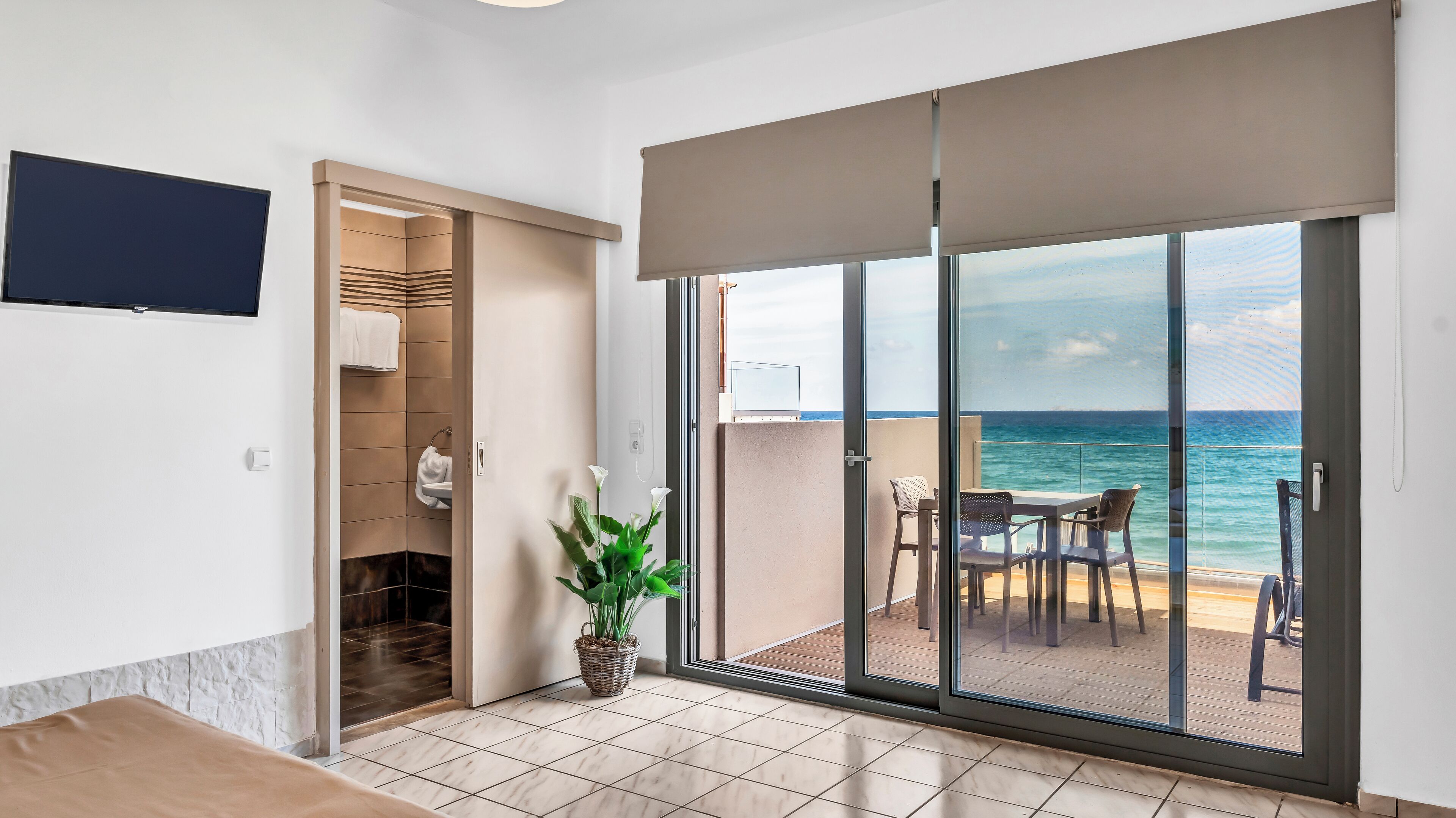 A room with a sliding glass door leading to a balcony with a view of the ocean.