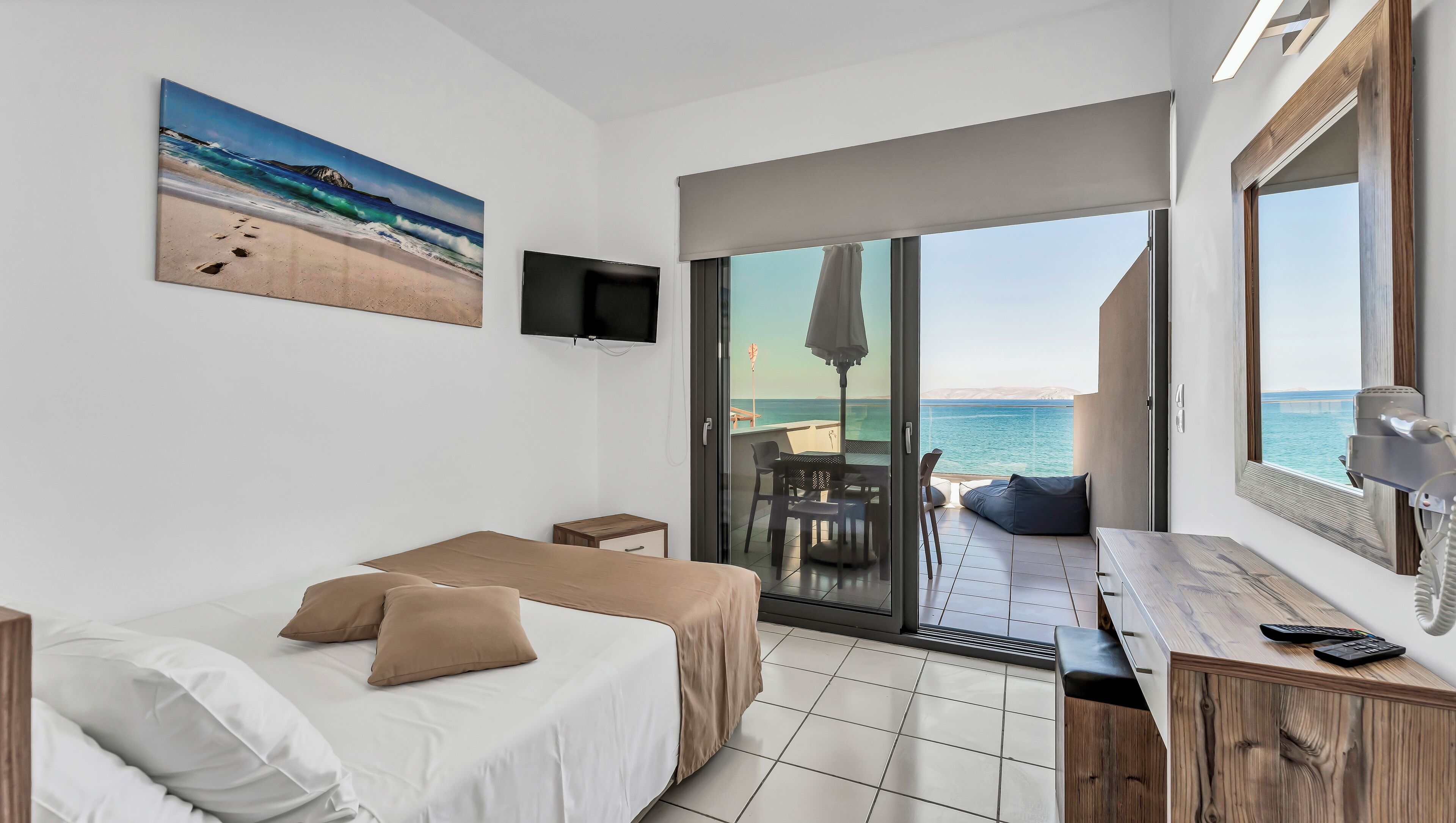 A hotel room with a bed, a desk, and a view of the sea through a sliding glass door.