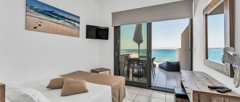 A hotel room with a bed, a desk, and a view of the sea through a sliding glass door.