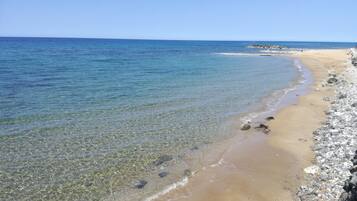 Una playa con agua cristalina, piedras y un promontorio rocoso a lo lejos.