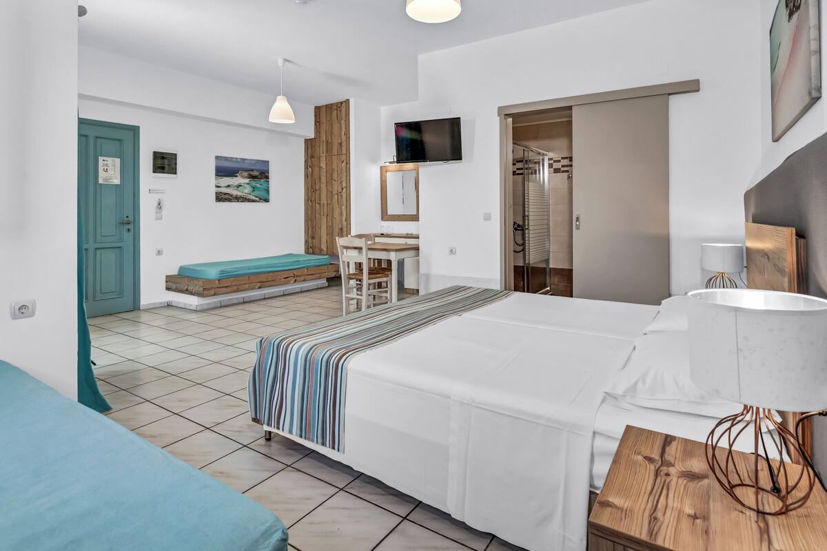 A hotel room with a bed, a desk, a chair, a TV, and a bathroom.