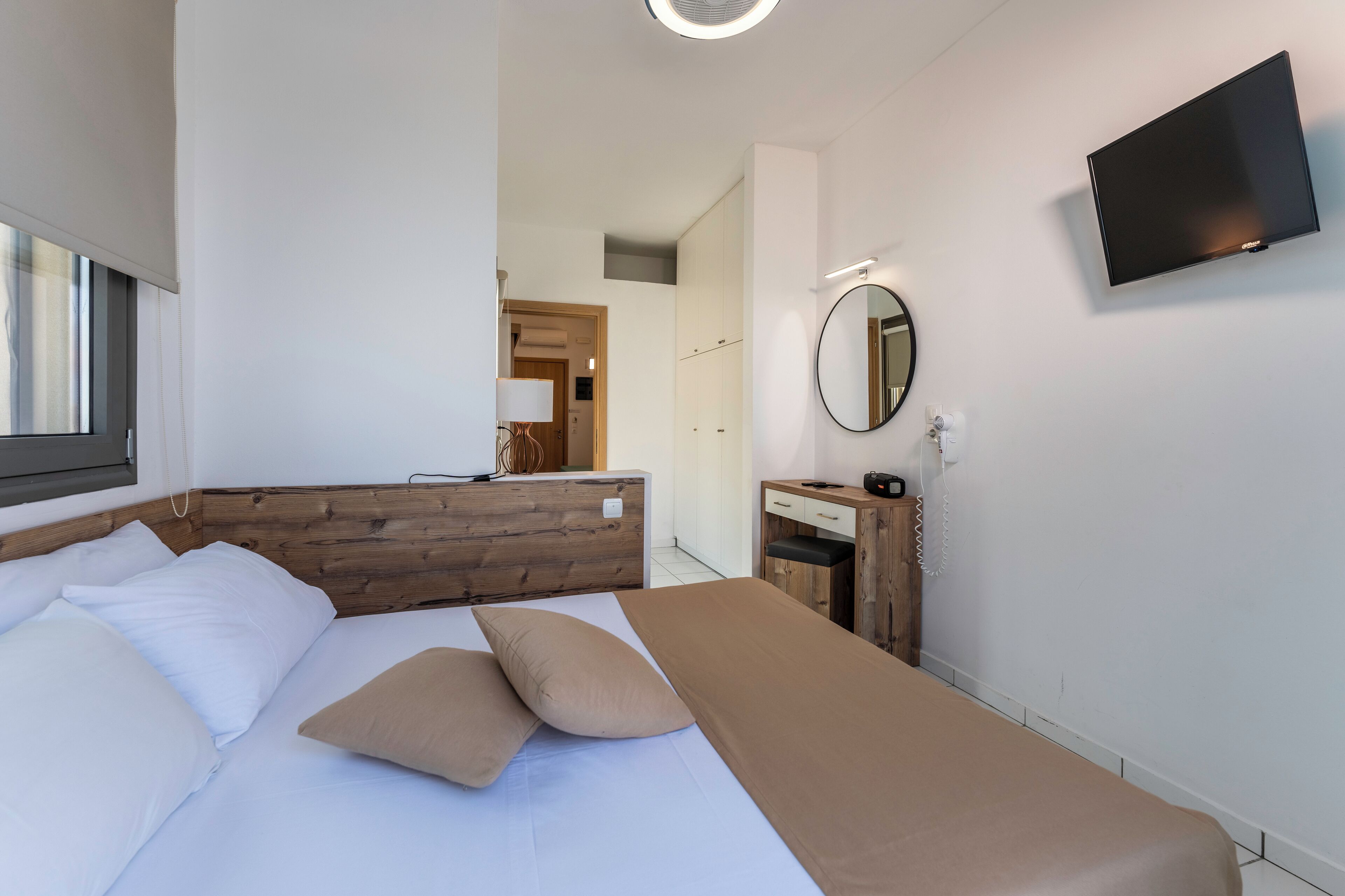 Een moderne hotelkamer met een groot bed, een houten hoofdbord, een nachtkastje met een lamp, een flatscreen televisie aan de wand en een spiegel.