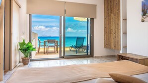 A bedroom with a bed, a potted plant, a sliding glass door leading to a balcony with a view of the sea, and a wooden bench. - Almare Beach Hotel (Hersonissos)