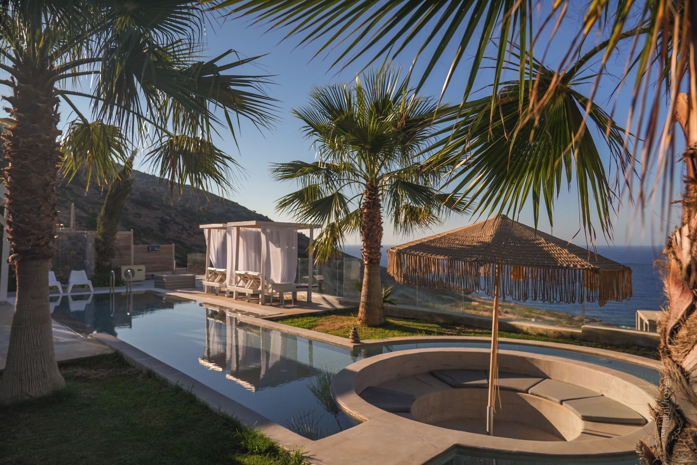 A pool area with a circular seating area, lounge chairs, and a covered seating area with a view of the sea.