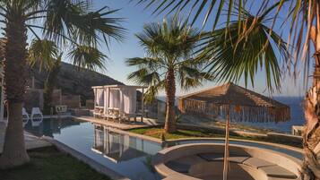 A pool area with a circular seating area, lounge chairs, and a covered seating area with a view of the sea.