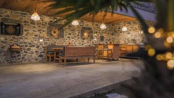 An outdoor dining area with stone walls, wooden furniture, and hanging pendant lights.