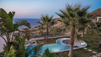 A pool area with palm trees and a view of the sea.