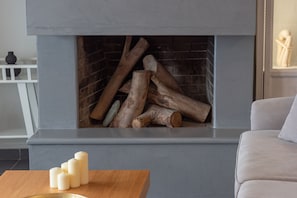 Un camino con legna, un divano bianco e un tavolo di legno con candele.