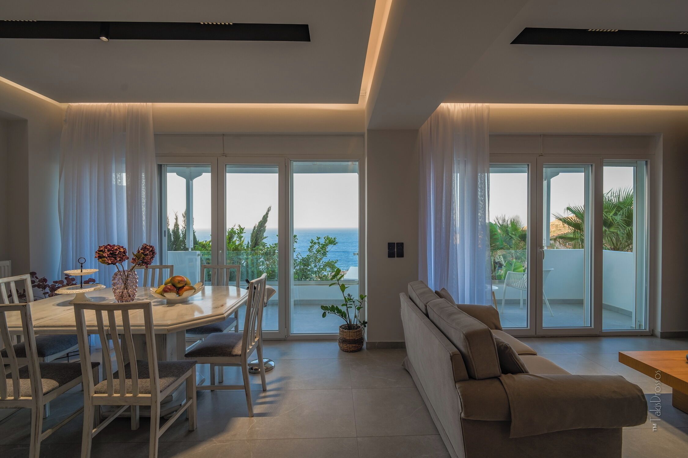 A modern living room with a dining area, large sliding glass doors, and a view of the sea.