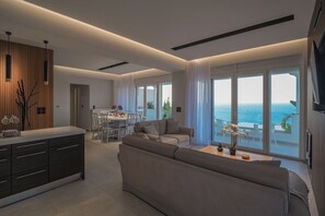 Un salon moderne comprenant un canapé, un coin repas et de grandes fenêtres offrant une vue sur la mer.