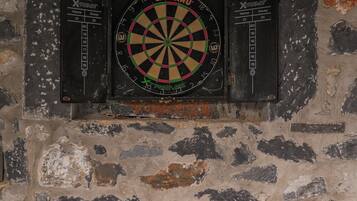 A dartboard mounted on a stone wall, a dartboard cabinet, and a basket with wooden paddles.