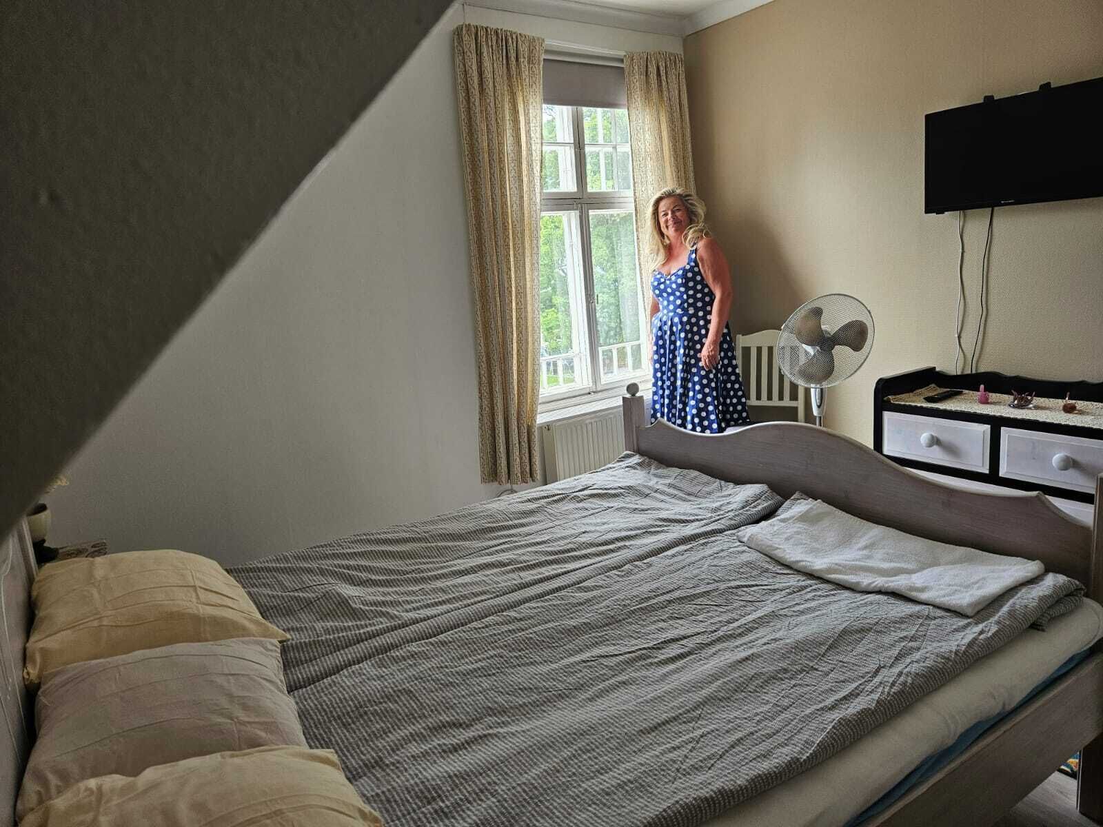 Un dormitorio con cama, cómoda, ventilador y ventana con cortinas.