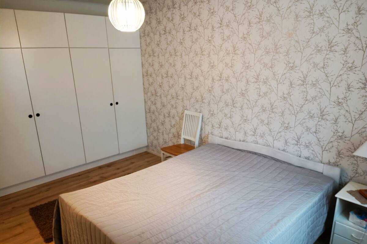 A bedroom with a large bed, a wardrobe, a chair, and a nightstand.