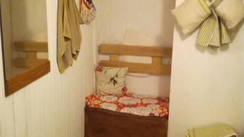 Een kleine, smalle kamer met een enkel bed, een houten hoofdbord, een radiator en een spiegel aan de linker muur.