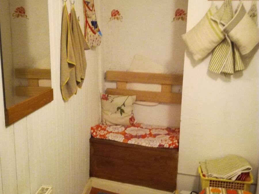 Een kleine, smalle kamer met een enkel bed, een houten hoofdbord, een radiator en een spiegel aan de linker muur.