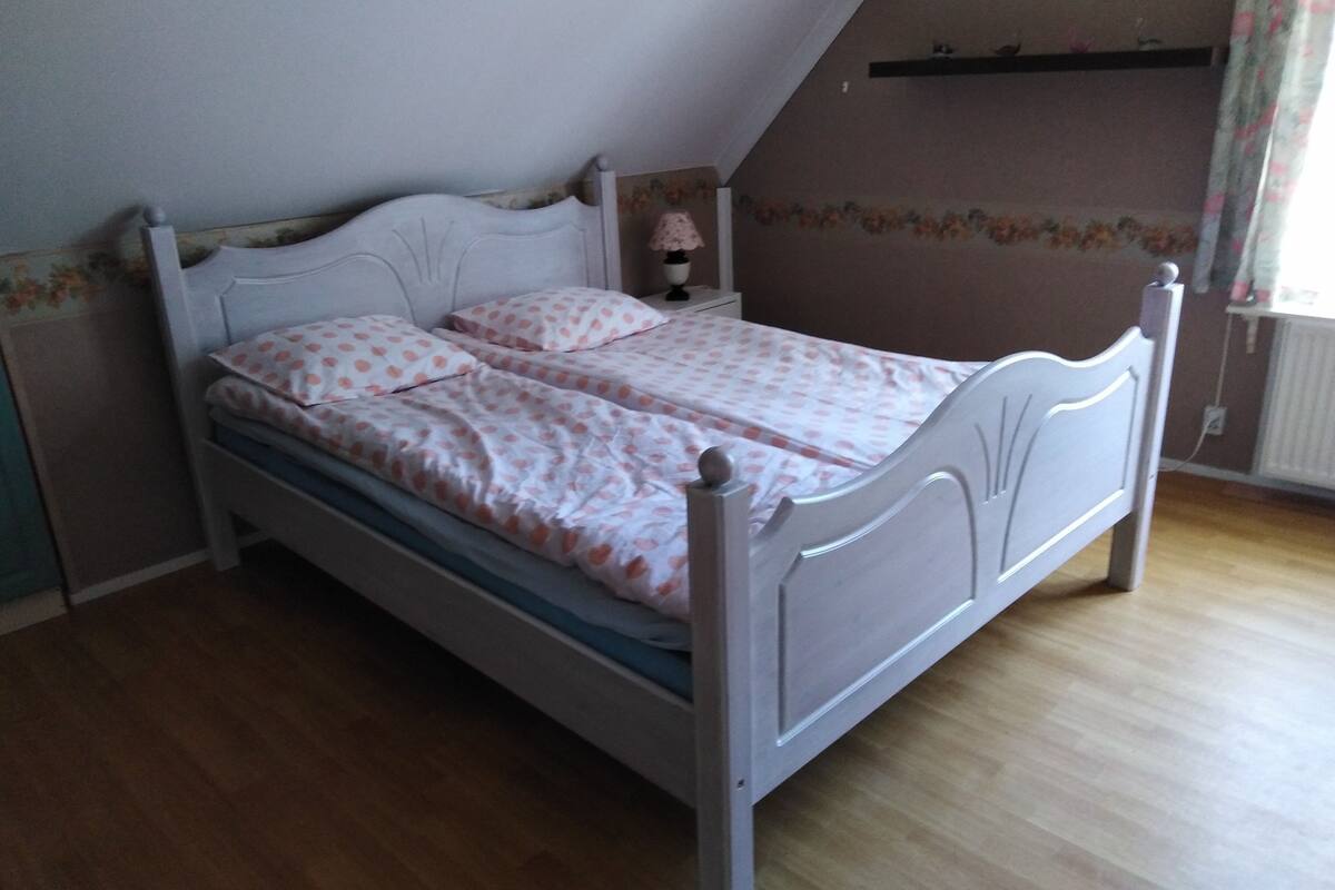 A single bed with a headboard, a bedside table with a lamp, and a floral-patterned wall.