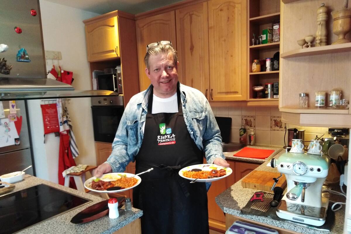 A kitchen with wooden cabinets, a vintage coffee maker, and a person holding plates of food.