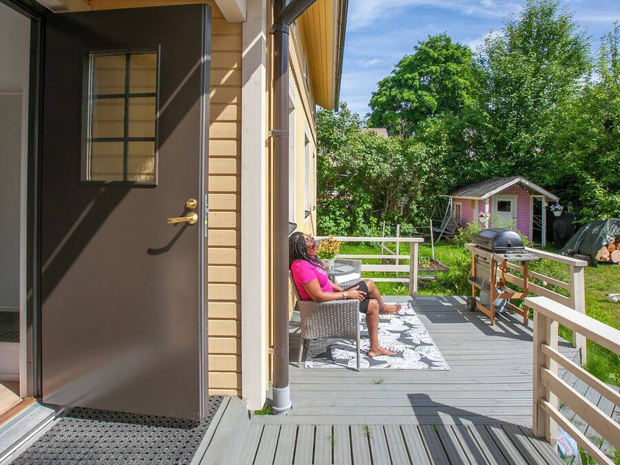 A woman sitting on a porch with a grill and a small shed in the background.
