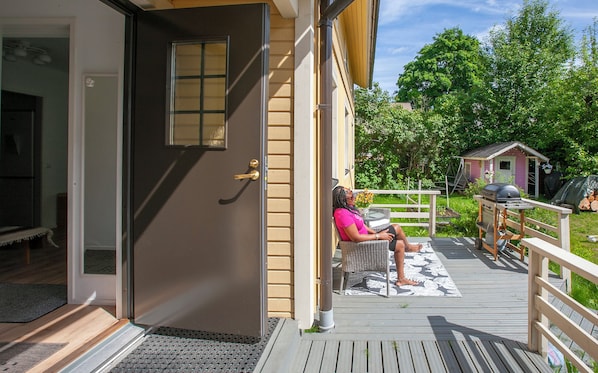 A woman sitting on a porch with a grill and a small shed in the background. - FirstHome GuestHouse (Jakobstad)