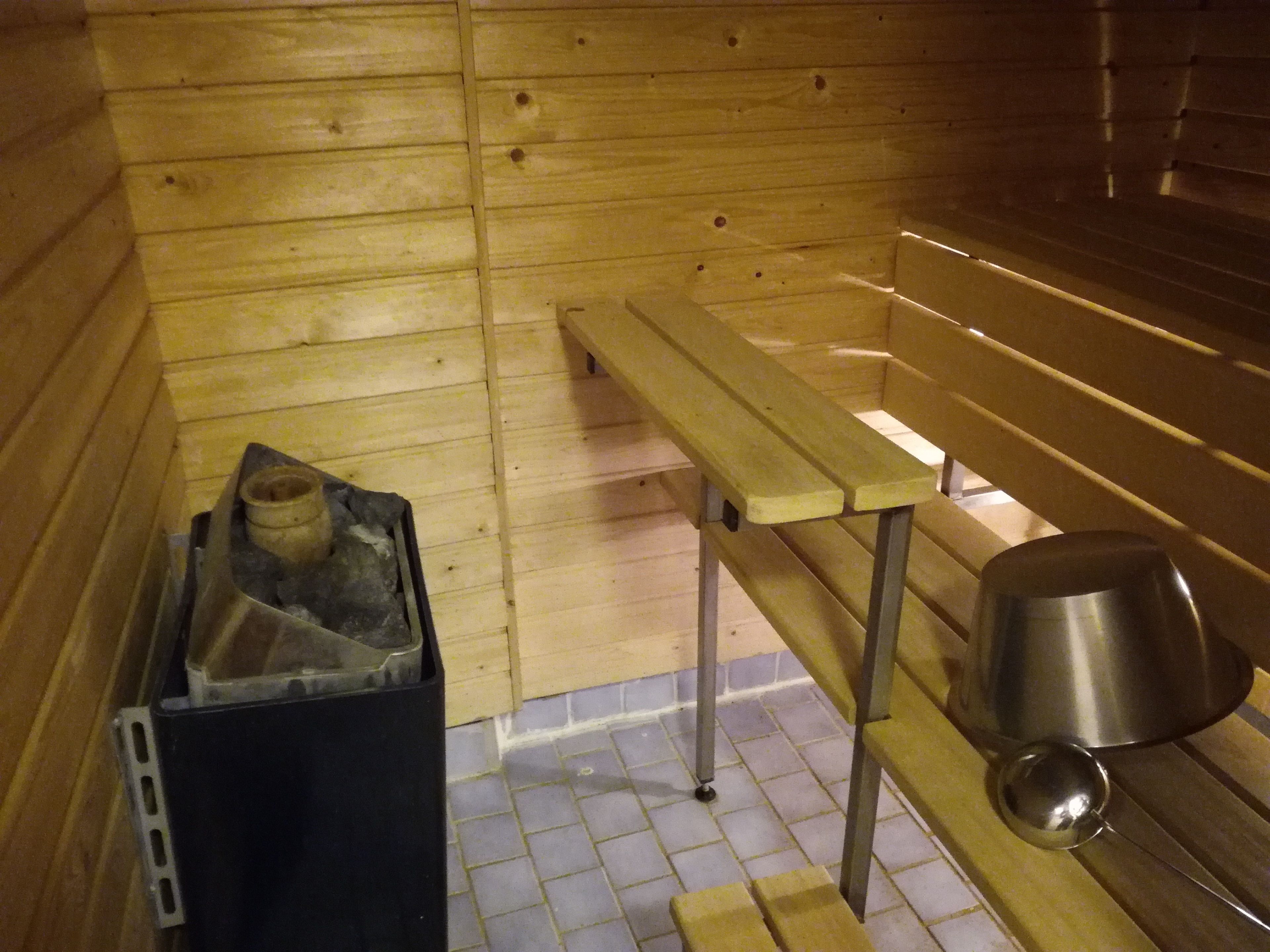 A sauna room with wooden benches, a bench heater, and a trash bin.