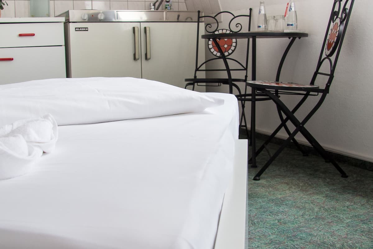 Une petite chambre propre, équipée d’un lit, d’un coin cuisine et d’un espace repas.
