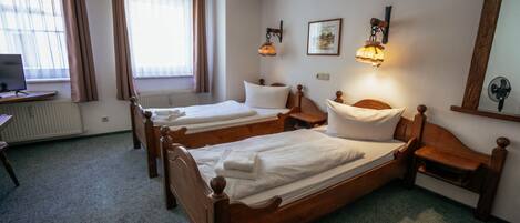 Habitación de hotel con dos camas de madera, un escritorio, una silla, un radiador y una ventana con cortinas.