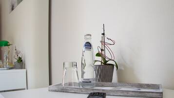 Eine Fernbedienung auf einem weißen Tisch mit einem Glas Wasser, einer Handdesinfektionsmittel-Flasche und einer Topfpflanze.
