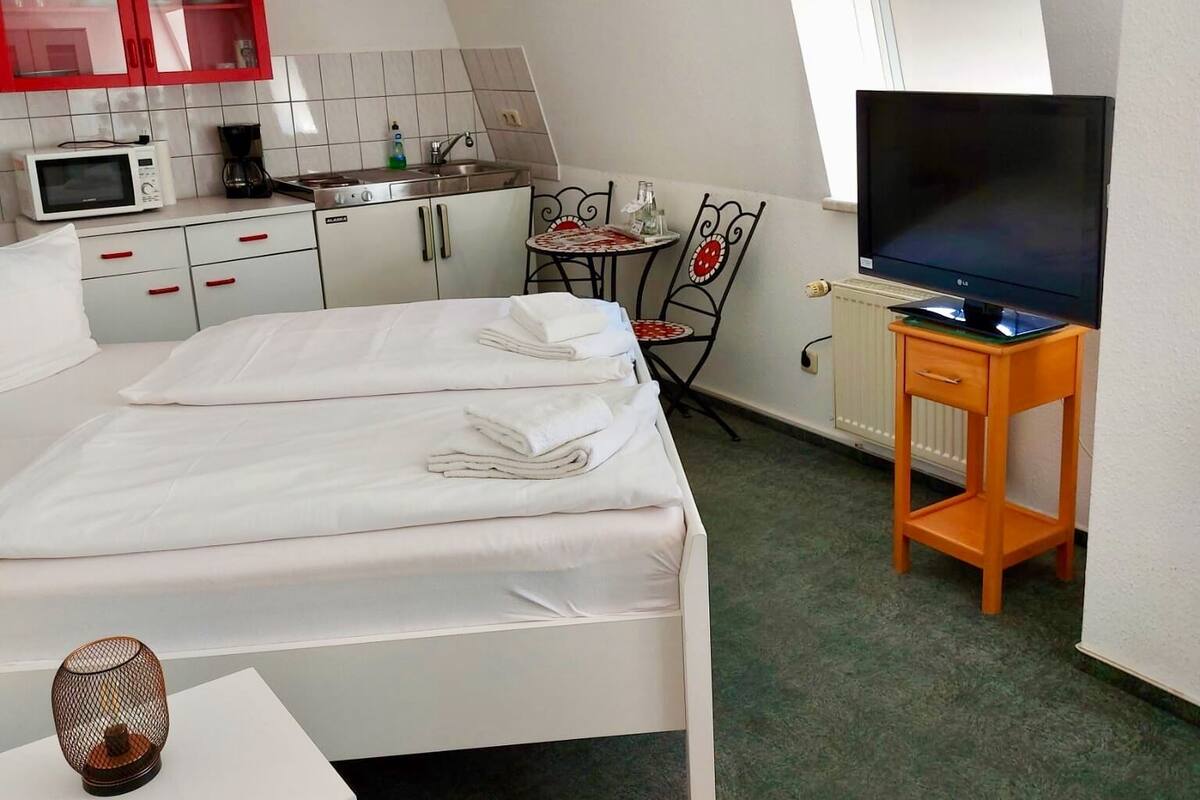 Une chambre d’hôtel compacte comprenant un lit, une télévision, une petite kitchenette et un coin repas.