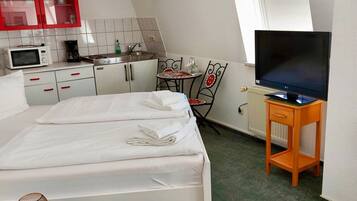 A compact hotel room with a bed, a TV, a small kitchenette, and a dining area.