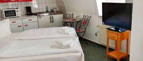 Una habitación de hotel compacta con cama, televisión, una kitchenette pequeña y un comedor.