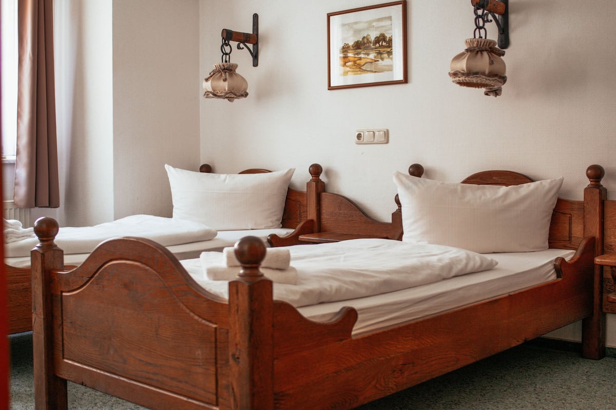 Un lit double en bois, avec du linge de lit et des oreillers blancs, une table de chevet et une lampe fixée au mur.