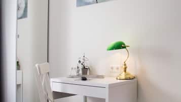 Ein weißer Schreibtisch mit einer grünen Schreibtischlampe, einem Stuhl und einem Spiegel.