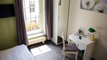 Un dormitorio con cama, escritorio, silla, ventana con cortinas, espejo y lámpara verde.