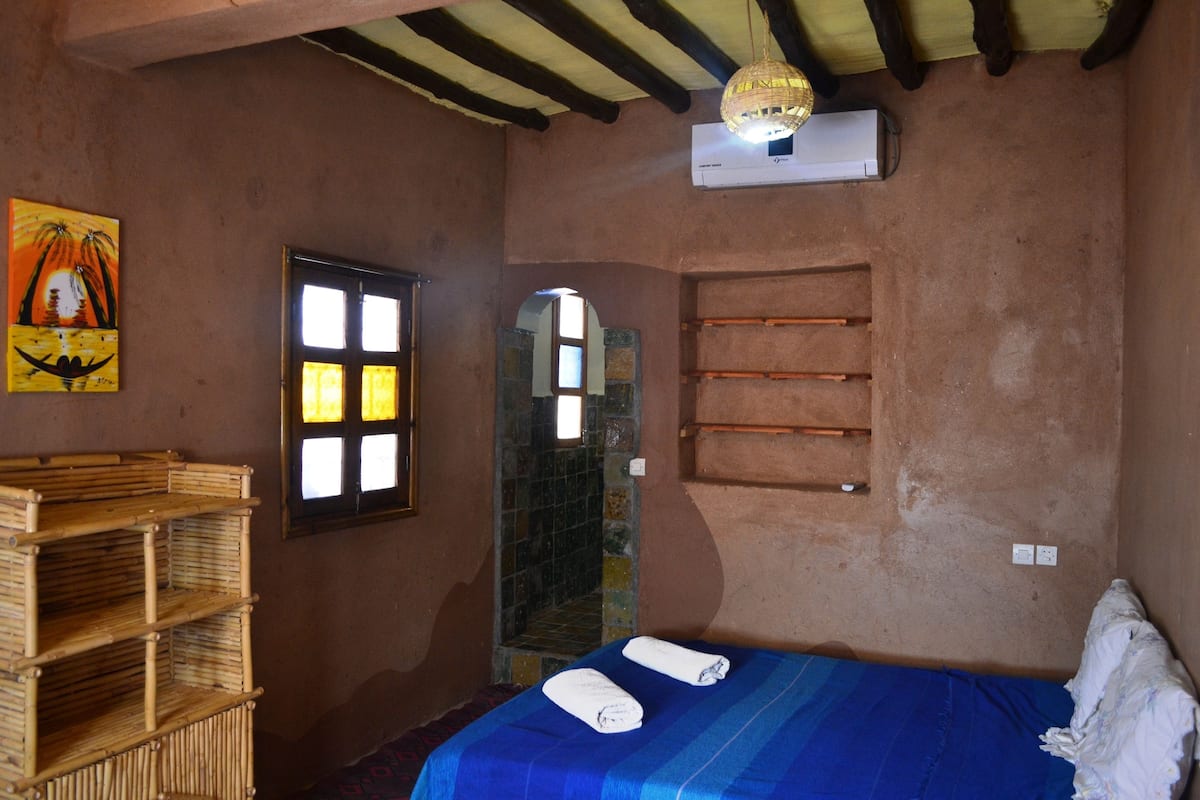 Een kamer met een bed, een raam, een wandplank en een bamboe kast.