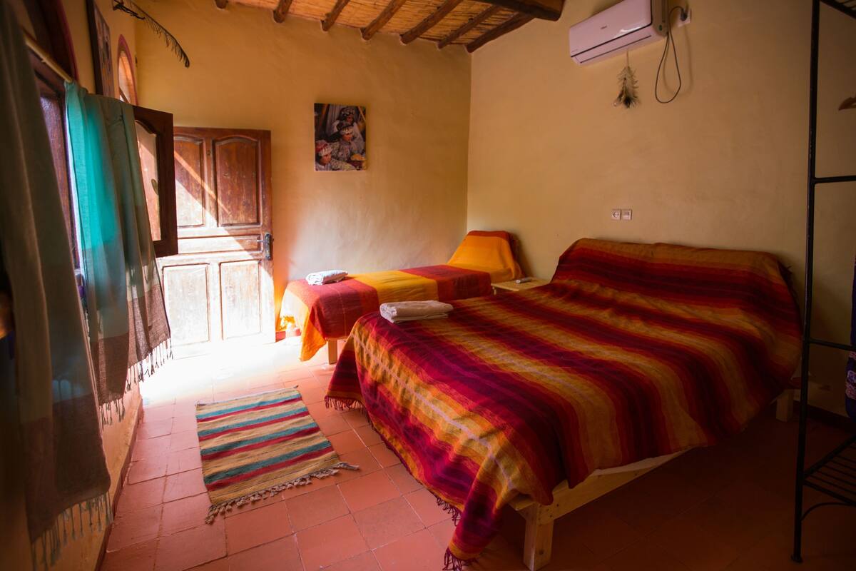Een kamer met een bed, een stoel, een raam, een deur en een wandgemonteerde airconditioner.