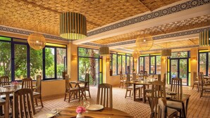 Ein Restaurant mit runden Tischen, Holzsesseln und großen Fenstern, die einen Blick ins Grüne bieten.