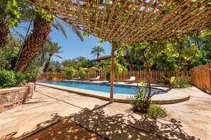Area piscina con un gazebo, palme e un recinto in legno.