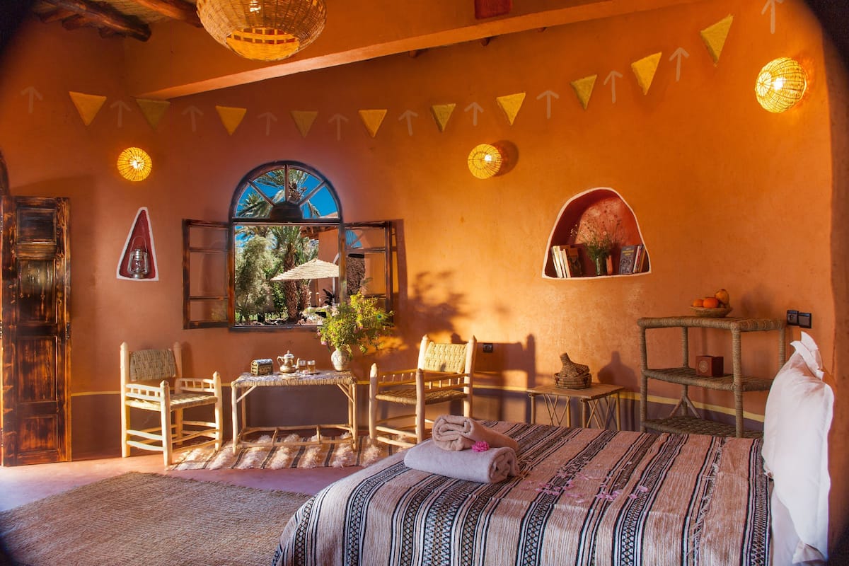Een kamer met een bed, stoelen, een tafel, een raam met uitzicht en wandplanken.