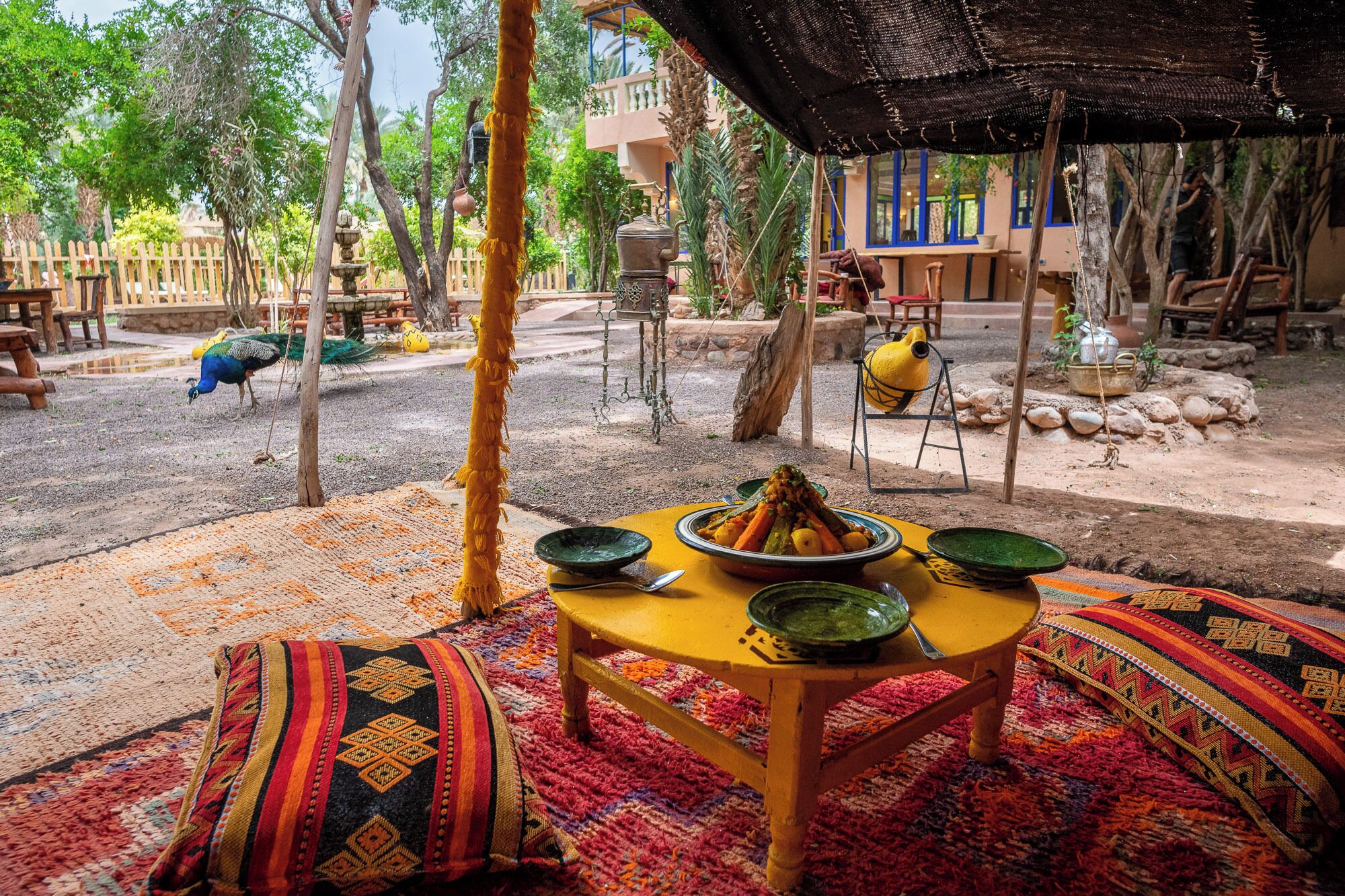Un espacio exterior de comedor tradicional con una mesa lista para una comida, rodeada de alfombras coloridas y una mesa de madera rústica.