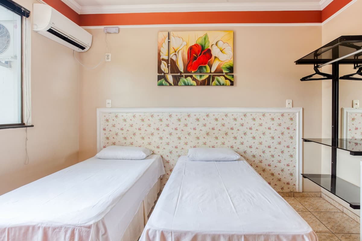 A room with two single beds, an air conditioning unit, a floral wallpaper, and a painting on the wall.