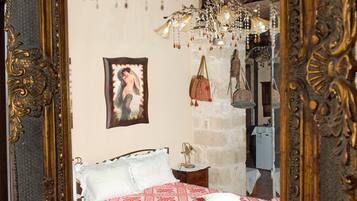 Une chambre à coucher avec un lit, un lustre, un tableau encadré au mur et un miroir doté d’un cadre orné.