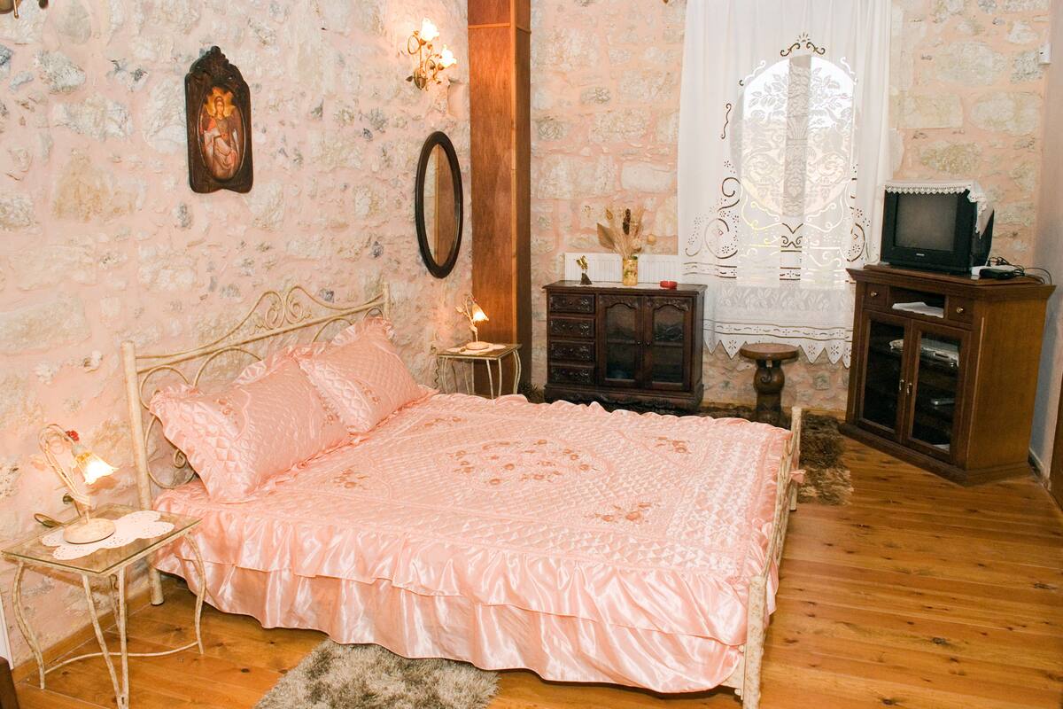 Une chambre à coucher avec un lit, une commode en bois, un téléviseur et un mur en pierre.