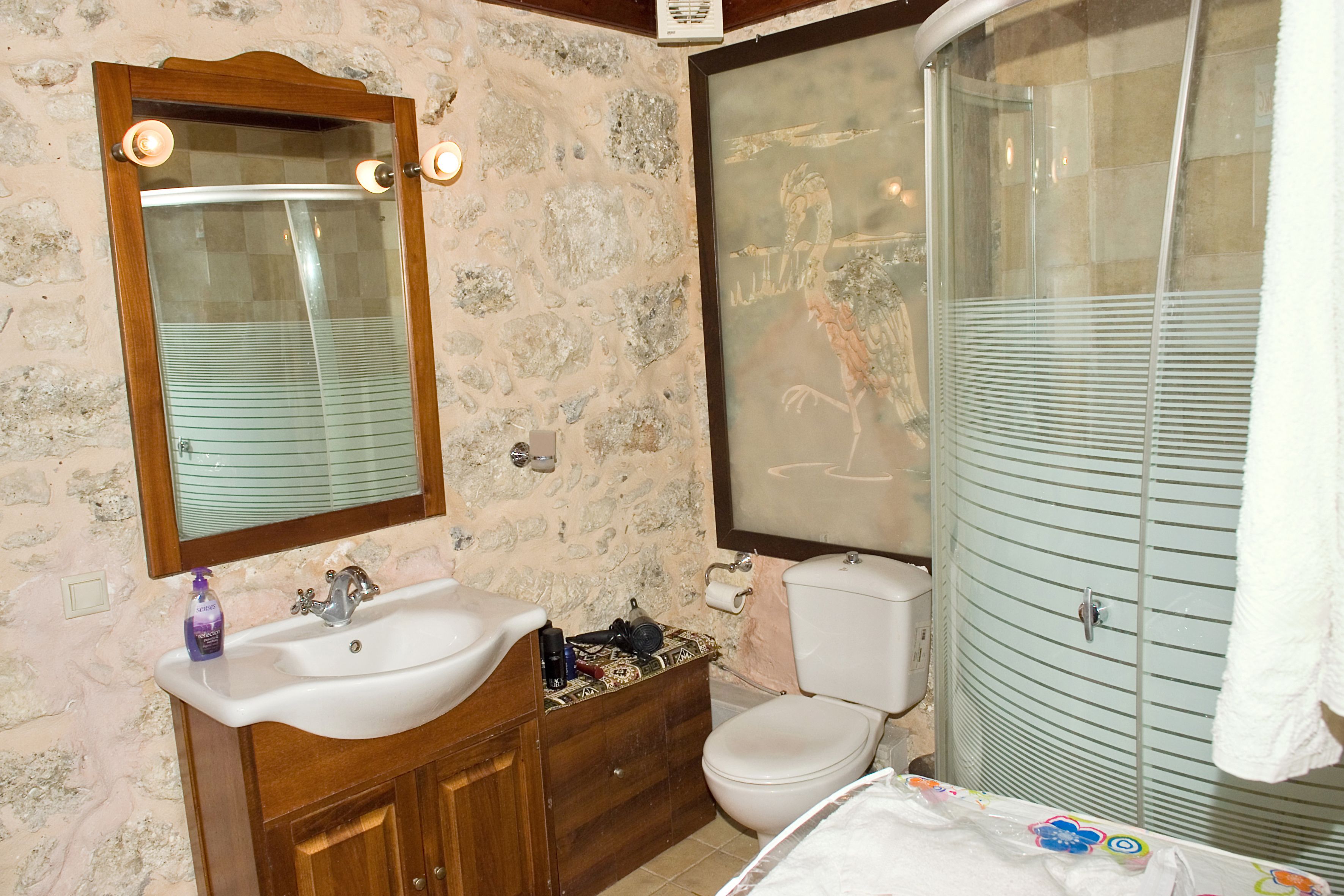 A bathroom with a stone wall, wooden vanity, white sink, and a glass shower enclosure.